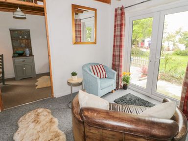 A living room with a leather sofa a blue armchair a small table with a plant a mirror on the wall and glass doors opening to a garden at Little House in Red Wharf Bay