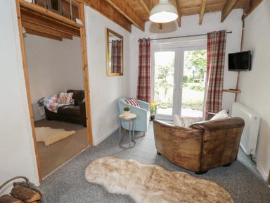 A sitting room with a leather armchair a blue chair a small table a mirror and a television at Little House in Red Wharf Bay