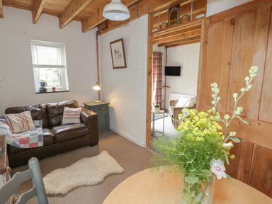 A sitting room with a brown leather sofa a small side table and a cream rug at Little House in Red Wharf Bay