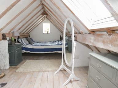 A bedroom with a bed striped bedding and a standing mirror in an attic at Little House in Red Wharf Bay