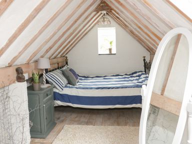 A bedroom with a bed striped bedding bedside table lamp and mirror at Little House in Red Wharf Bay