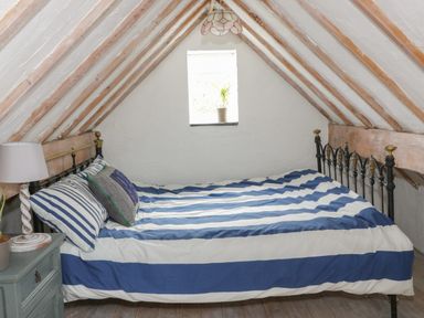 A small attic bedroom with a bed with striped bedding and a nightstand with a lamp at Little House in Red Wharf Bay