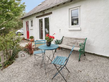 An outdoor patio area with a blue metal table and chairs a wooden bench and potted plants at Little House in Red Wharf Bay