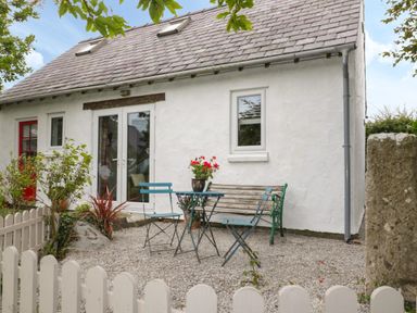 A small outdoor seating area with a table two chairs and a bench in front of a white house with a red door at Little House in Red Wharf Bay