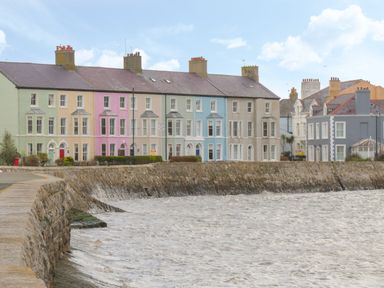 A row of pastel colored houses along a waterfront with a stone sea wall at Little House in Red Wharf Bay