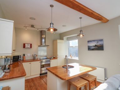 A kitchen with wooden countertops an island with stools two pendant lights a stove and a window at 1 Bailey's Cottage in Stoke Fleming