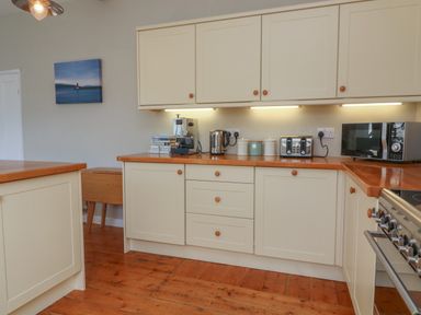 A kitchen with wooden floors cream cabinets and appliances including a toaster kettle and microwave at 1 Bailey's Cottage in Stoke Fleming