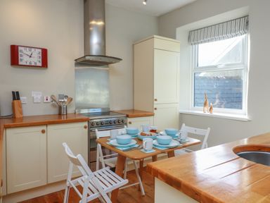 A kitchen with wooden countertops a dining table set for four and a window at 1 Bailey's Cottage in Stoke Fleming