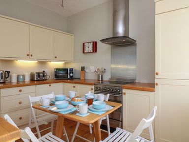 A kitchen with a wooden table set for breakfast and cream cabinets at 1 Bailey's Cottage in Stoke Fleming