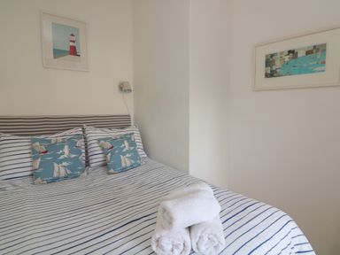 A bedroom with a striped bedspread pillows with sailboat designs two framed pictures and folded white towels on the bed at 1 Bailey's Cottage in Stoke Fleming