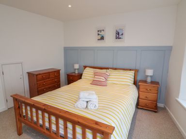 A bedroom with a wooden bed frame yellow striped bedding two framed pictures bedside tables and lamps at 1 Bailey's Cottage in Stoke Fleming