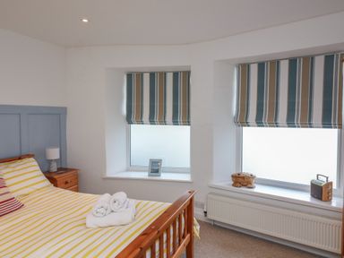 A bedroom with a wooden bed and striped window blinds at 1 Bailey's Cottage in Stoke Fleming