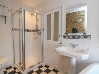 A bathroom with a glass shower enclosure a white pedestal sink a mirror above the sink and a checkered floor at 1 Bailey's Cottage in Stoke Fleming