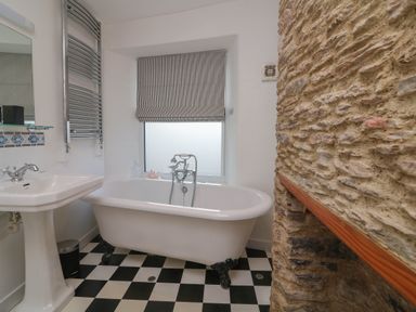A bathroom with a clawfoot bathtub a pedestal sink and a stone wall at 1 Bailey's Cottage Stoke Fleming