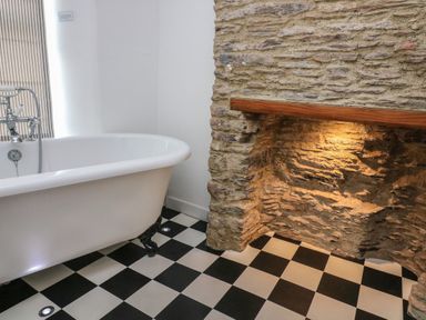 A bathroom with a clawfoot bathtub and a stone fireplace with lighting at 1 Bailey's Cottage in Stoke Fleming