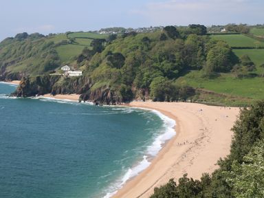 A sandy beach with people near the shoreline and green hills in the background at 1 Bailey's Cottage in Stoke Fleming