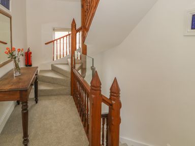 A carpeted staircase with wooden railings and a wooden table with flowers in a vase at Preswylfa in Caernarfon
