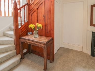 A wooden table with a jar of yellow flowers next to a carpeted staircase with wooden railing at Preswylfa in Caernarfon