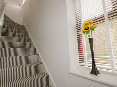 A staircase with striped carpet and a window with blinds and a vase of sunflowers on the windowsill at Elin Howlyek in Newquay