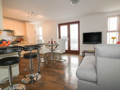 An open plan kitchen and living room with bar stools a dining table and a wall mounted television at Elin Howlyek in Newquay