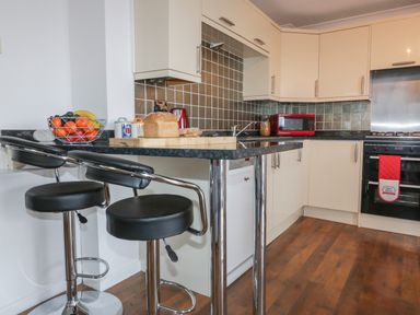 A kitchen with a breakfast bar and stools a fruit bowl bread toaster microwave and oven at Elin Howlyek in Newquay