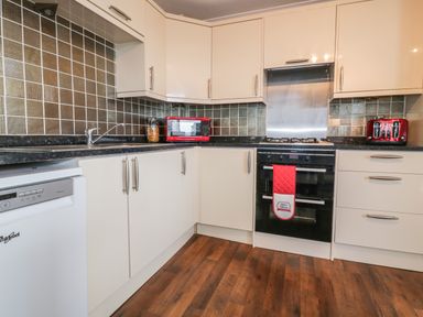 A kitchen with white cabinets black countertops red microwave and toaster black oven and wooden floor at Elin Howlyek in Newquay