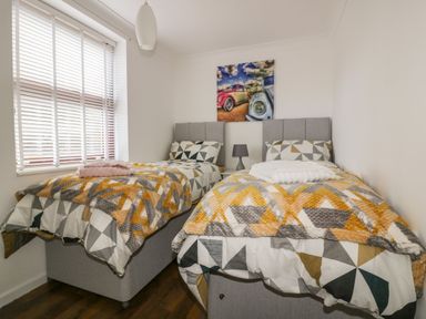 A bedroom with two single beds patterned bedding and a small lamp on a nightstand at Elin Howlyek in Newquay