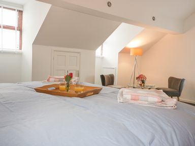 A bedroom with a bed holding a tray with glasses of orange juice and a rose at Elin Howlyek in Newquay