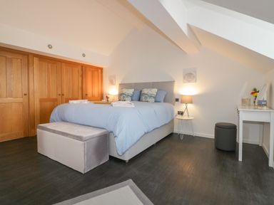 A bedroom with a bed a bench at the foot of the bed a side table with a lamp and a dressing table with a stool at Elin Howlyek in Newquay