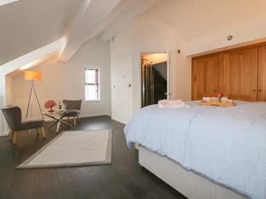 A bedroom with a bed a glass table two chairs a floor lamp and wooden wardrobes at Elin Howlyek in Newquay