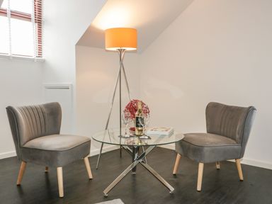 A sitting area with two grey chairs a glass coffee table a floor lamp and a bottle of wine at Elin Howlyek in Newquay