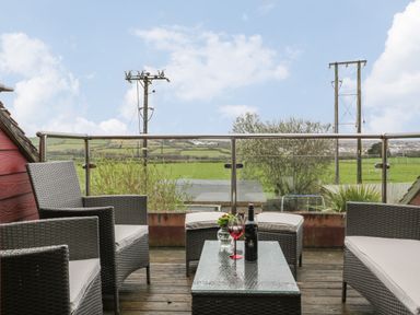 Outdoor seating area with wicker chairs and table on a wooden deck overlooking fields at Elin Howlyek in Newquay