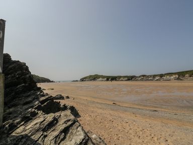 A sandy beach with rocky outcrops under a clear sky at Elin Howlyek in Newquay