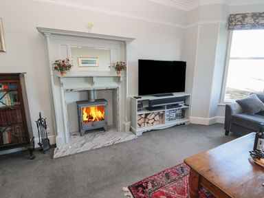 A living room with a fireplace TV stand with a TV and firewood and a coffee table at Whinstones at 4 The Villas in Embleton