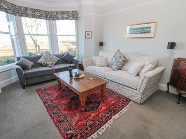 A living room with two sofas a wooden coffee table and a red patterned rug at Whinstones at 4 The Villas in Embleton