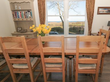 A dining room with wooden table and chairs a vase with yellow flowers and a bookcase at Whinstones at 4 The Villas in Embleton
