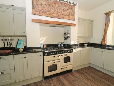 A kitchen with beige cabinets a black countertop a cream colored double oven stove mounted knives and a tapestry above the stove at Whinstones at 4 The Villas in Embleton