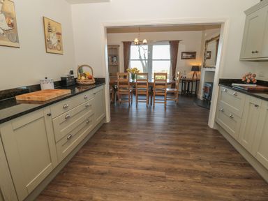 A kitchen with cabinets counters and a cutting board leading to a dining area with a table and chairs at Whinstones at 4 The Villas in Embleton