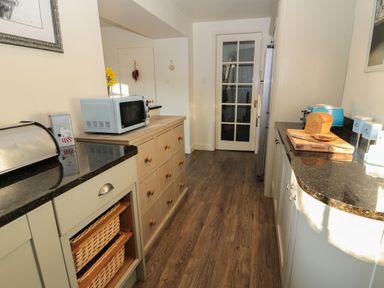A kitchen with wooden cabinets a microwave sliced bread on a cutting board and a glass door at Whinstones at 4 The Villas Embleton