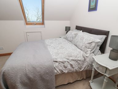 A bedroom with a double bed beside two bedside tables with lamps under a skylight window at Whinstones at 4 The Villas in Embleton