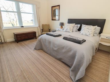 A bedroom with a double bed two bedside tables a chair and a wooden chest by the window at Whinstones at 4 The Villas in Embleton