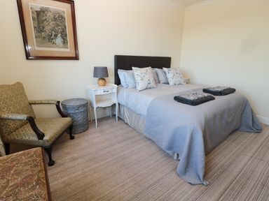 A bedroom with a bed with pillows and folded blankets bedside tables lamp armchairs a basket and artwork on the wall at Whinstones at 4 The Villas Embleton