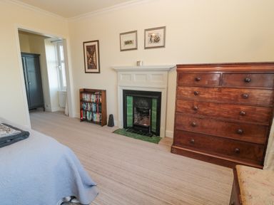 A bedroom with a wooden chest of drawers a small bookshelf a fireplace and a bed at Whinstones at 4 The Villas in Embleton