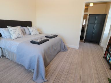 A bedroom with a bed with pillows and folded towels a dark wardrobe and a bookshelf at Whinstones at 4 The Villas in Embleton
