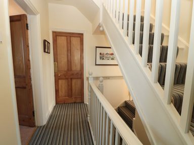 A hallway with wooden doors and striped carpeted stairs at Whinstones at 4 The Villas in Embleton