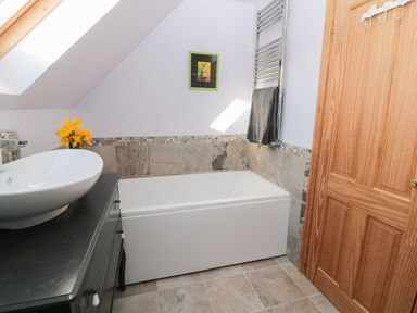 A bathroom with a bathtub sink flowers and a towel on a radiator at Whinstones at 4 The Villas Embleton