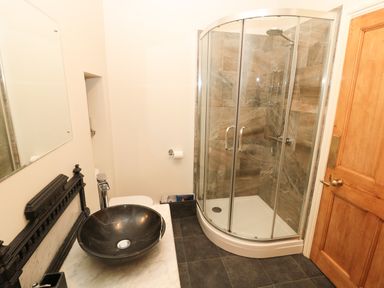 A bathroom with a circular black basin on a marble countertop a glass shower enclosure and a wooden door at Whinstones at 4 The Villas in Embleton