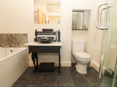 A bathroom with a bathtub sink on a wooden vanity toilet and a glass shower at Whinstones at 4 The Villas Embleton