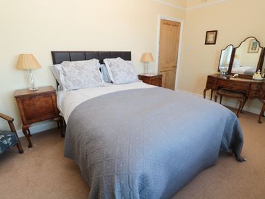 A bedroom with a bed a wooden dressing table and two bedside tables with lamps at Whinstones at 4 The Villas in Embleton