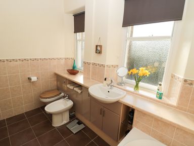 A bathroom with a toilet bidet sink mirror flowers and a window at Whinstones at 4 The Villas in Embleton